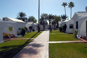 A pathway leading to a row of white buildings with palm trees and a clear sky. - Canary Garden Club (San Bartolomé de Tirajana)