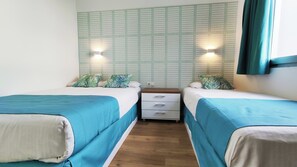 Ein Zimmer mit zwei Betten, jeweils mit blauer Bettdecke und weißen Kissen, neben einer Wand mit Gittermuster und zwei Wandleuchten.