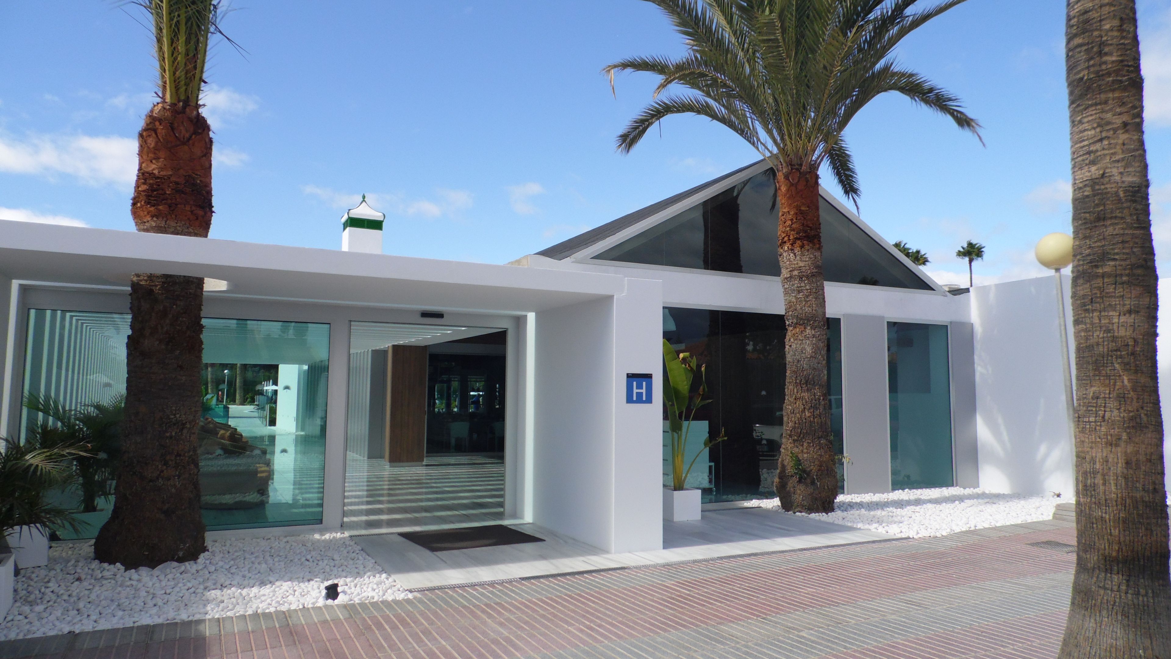 A modern building with a glass entrance, palm trees, and a clear sky.