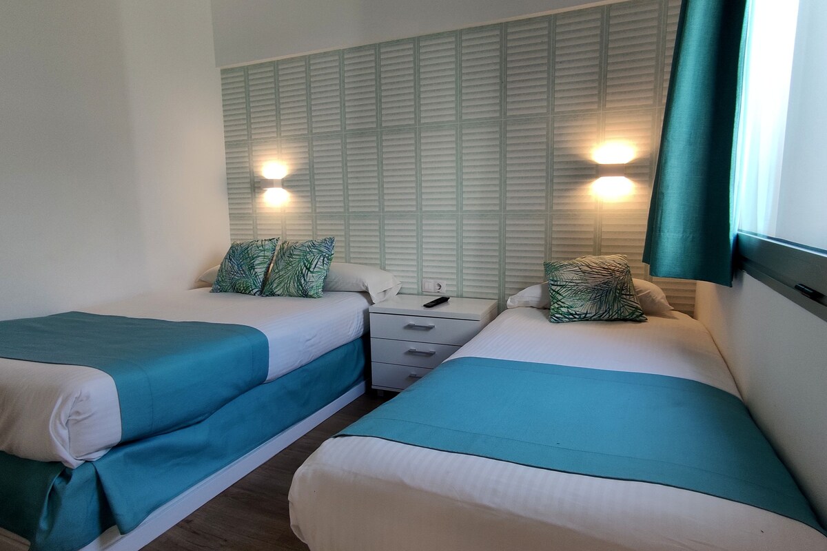 Twin beds with teal bedding, a nightstand, and wall-mounted lights.