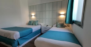 Twin beds with teal bedding, a nightstand, and wall-mounted lights. - Canary Garden Club (San Bartolomé de Tirajana)