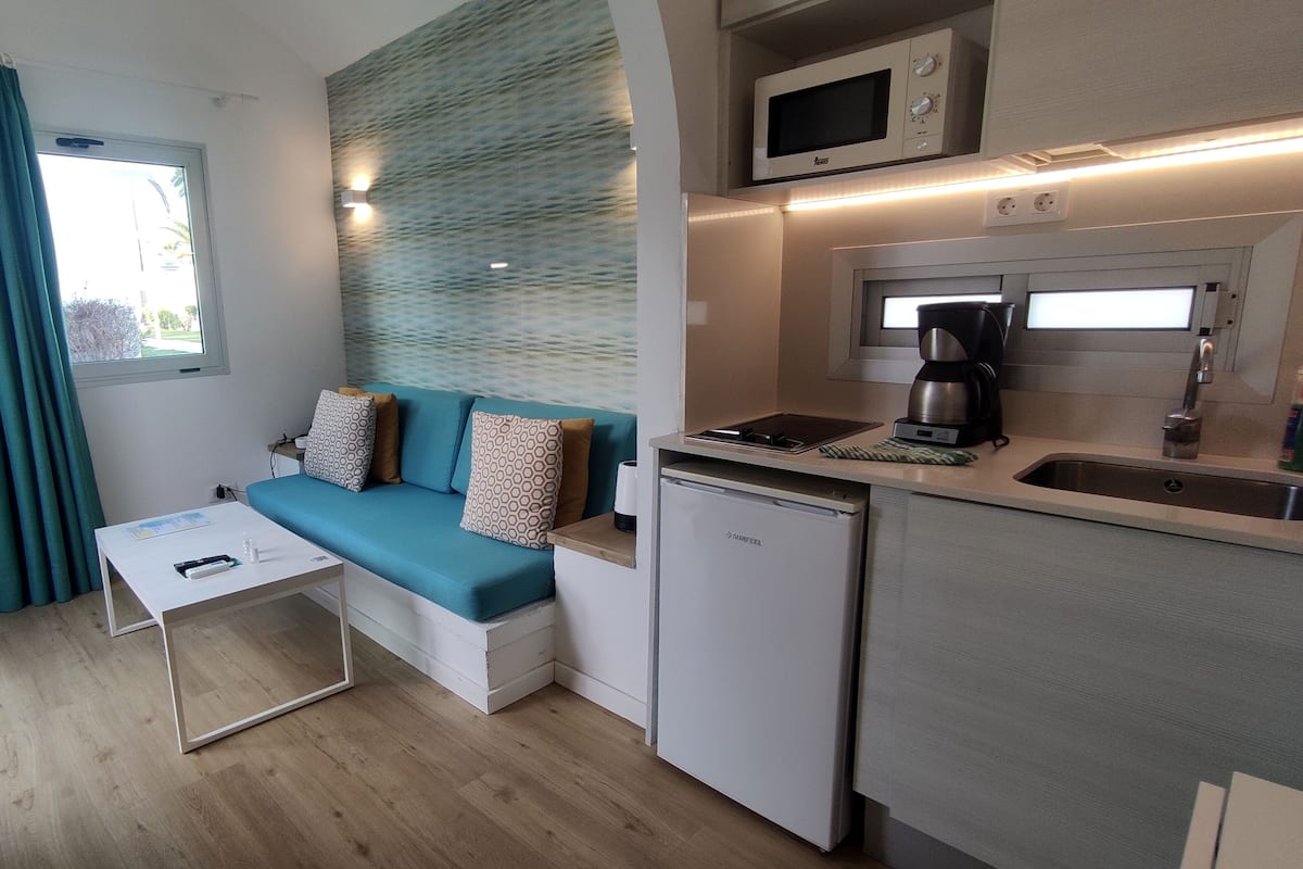Un espacio habitable pequeño con sofá, una mesita, microondas, cafetera y refrigerador pequeño.