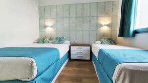 A room with two beds, each with a blue bedspread and white pillows, flanked by a wall with a grid pattern and two wall-mounted lights. - Canary Garden Club (San Bartolomé de Tirajana)