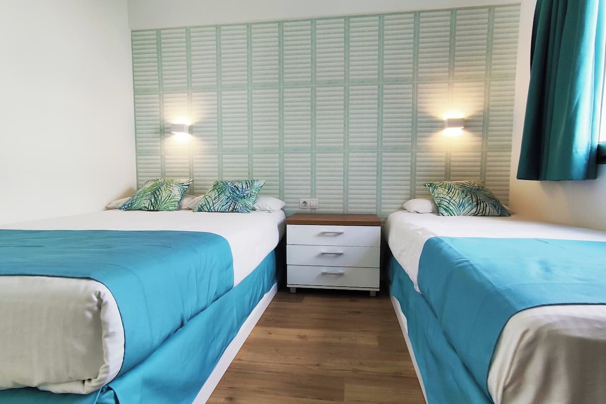 Una habitación con dos camas, cada una con cubrecama azul y almohadas blancas, flanqueada por una pared con diseño de cuadrícula y dos luces fijadas a la pared.