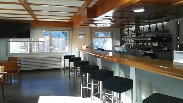 A bar area with a wooden counter, bar stools, and a shelf with bottles. - Apartamentos Solneu (Naut Aran)
