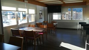 A spacious dining area with multiple tables and chairs, large windows with city views, and a modern ceiling design. - Apartamentos Solneu (Naut Aran)