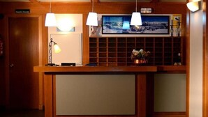 A reception desk with a wooden finish, two pendant lights, a television above the desk, and a small plant on the right. - Apartamentos Solneu (Naut Aran)