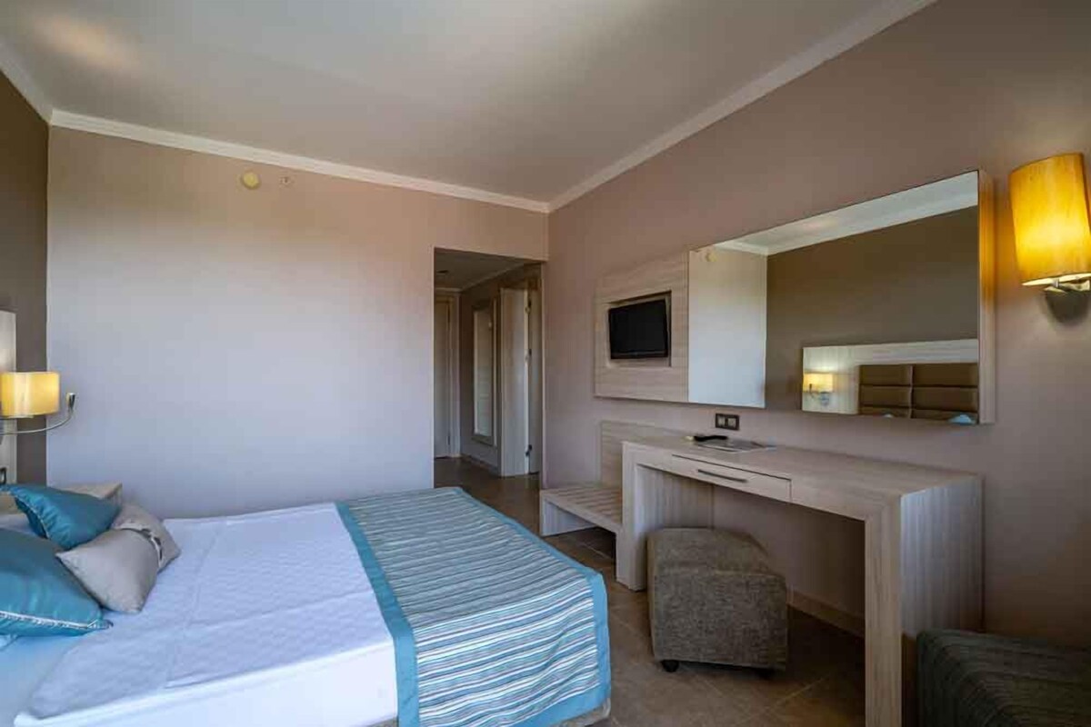 A hotel room with a bed, a desk, a chair, a television, and a lamp.
