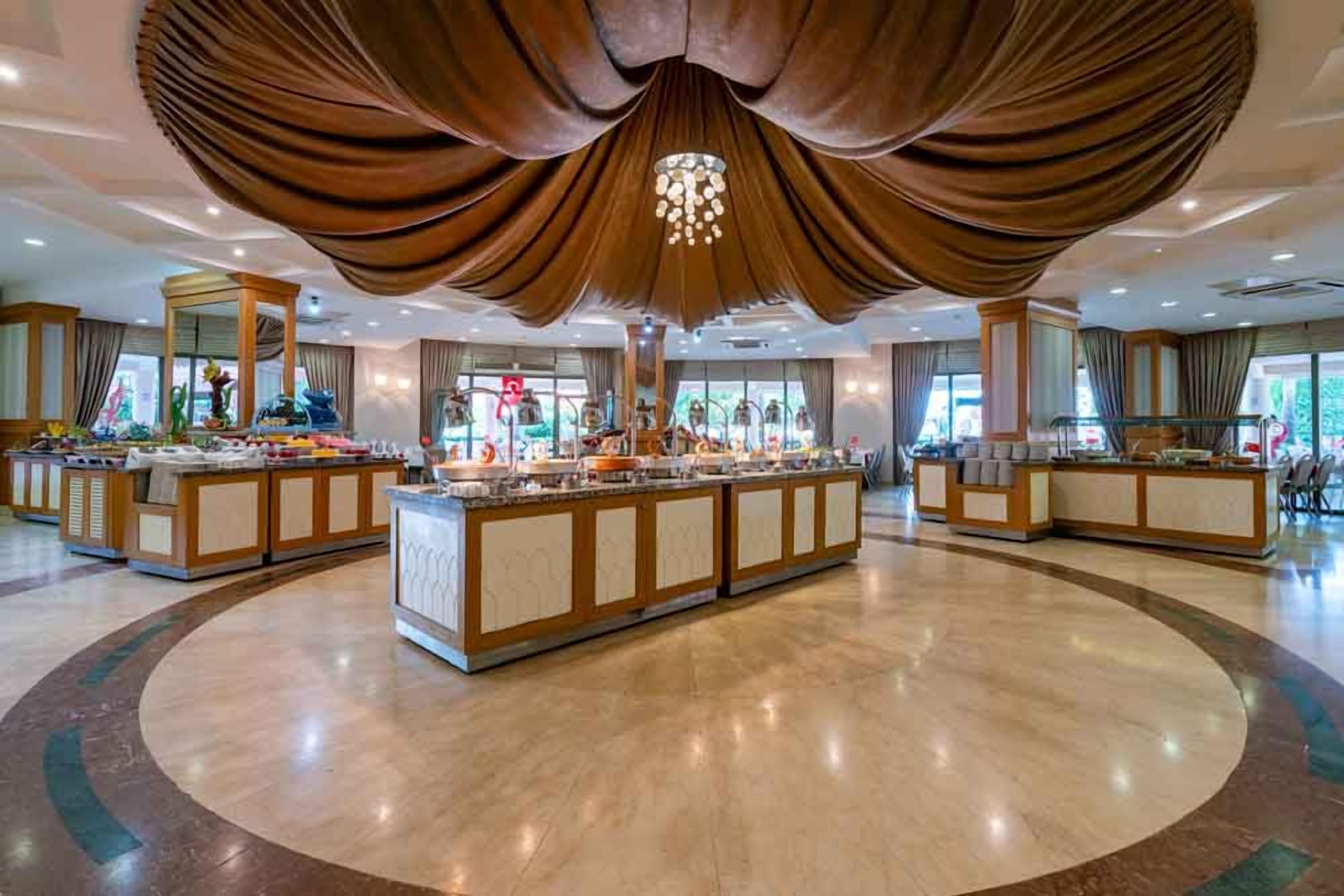 Eine geräumige Hotelhalle mit einer zentralen Buffet-Ecke, verschiedenen Sitzgelegenheiten und einer großen Kronleuchter.