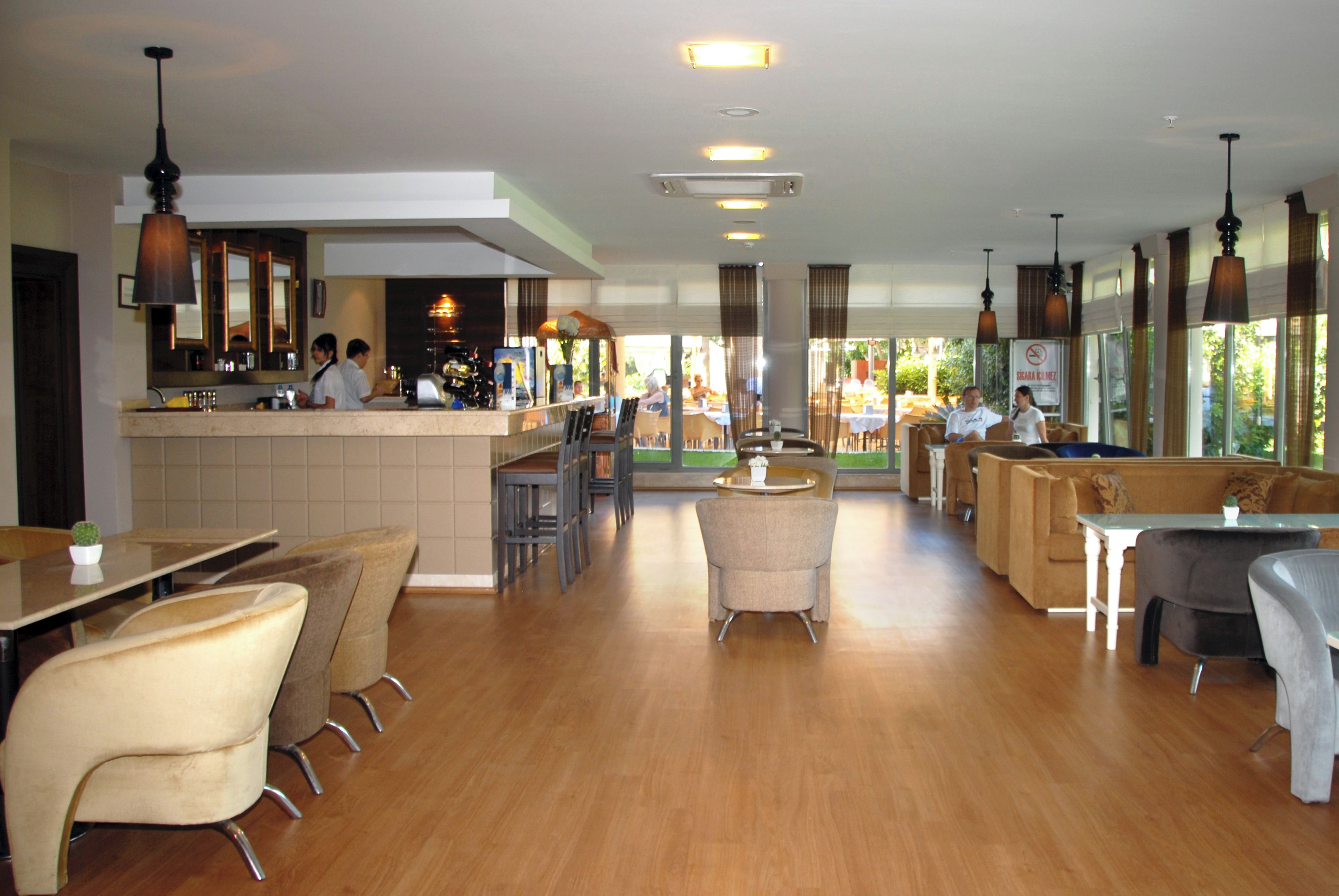Ein geräumiges Restaurant mit Barbereich, verschiedenen Sitzgelegenheiten wie Sitzecken und Tischen sowie Blick ins Freie durch große Fenster.
