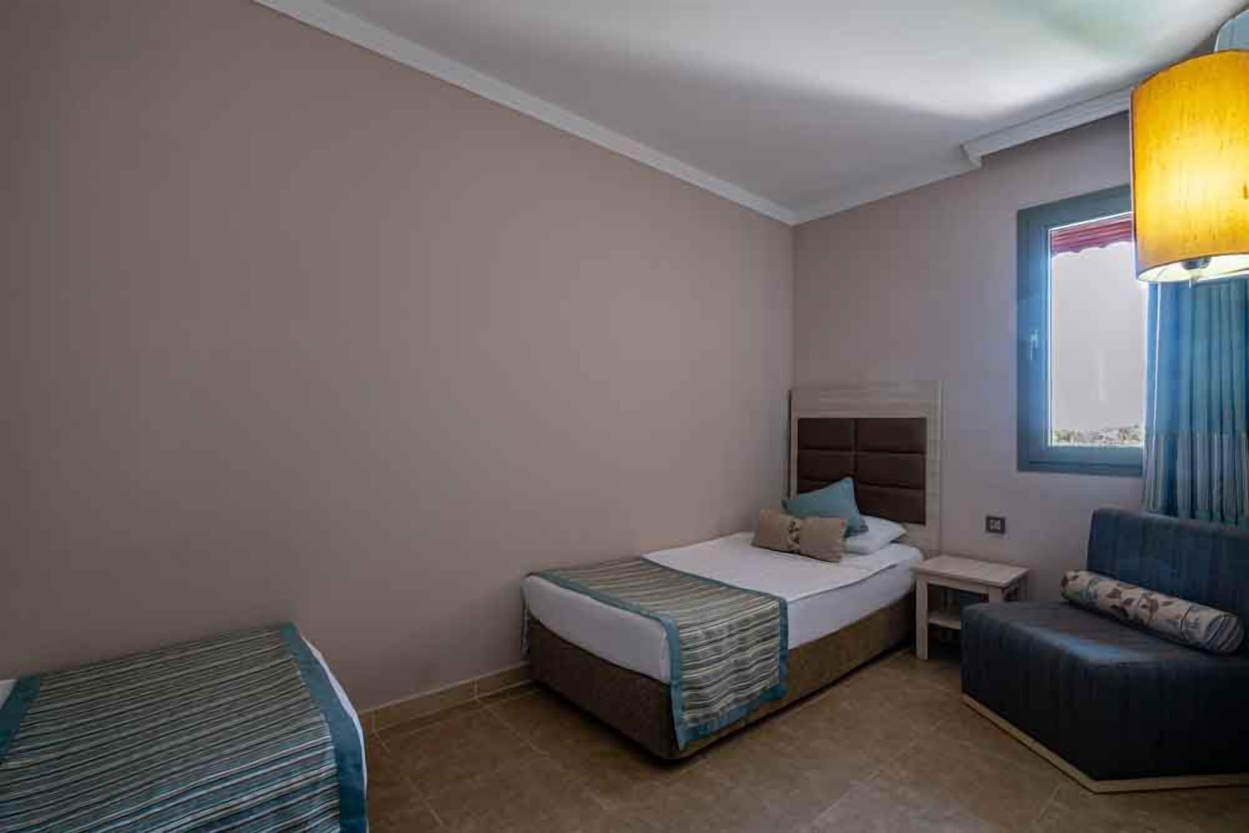 Ein Hotelzimmer mit Bett, einem kleinen Tisch, einem Stuhl und einem fenster mit Vorhängen.