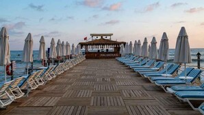 A wooden deck with rows of sun loungers and umbrellas, leading to a shaded area with a sign reading "PALMERAS". - Palmeras Beach Hotel (Alanya)