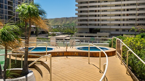 A rooftop pool area with hot tubs, surrounded by palm trees and a view of a cityscape.