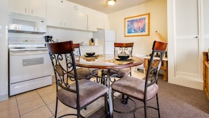 A compact kitchen with white cabinets, a microwave, an oven, and a dining table with four chairs.