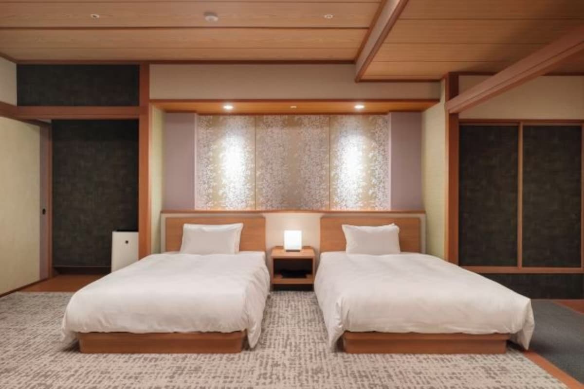 A hotel room with two beds, a nightstand, a wall-mounted lamp, and a patterned wall.
