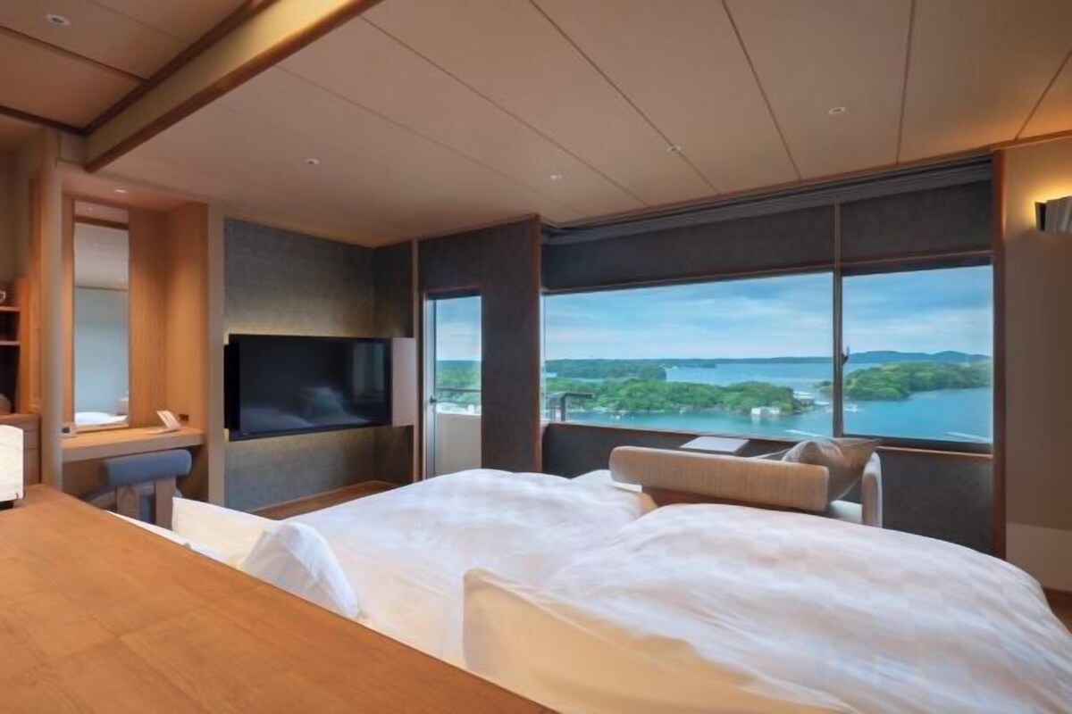 A hotel room with a large bed, a TV, a desk, and a view of a body of water.