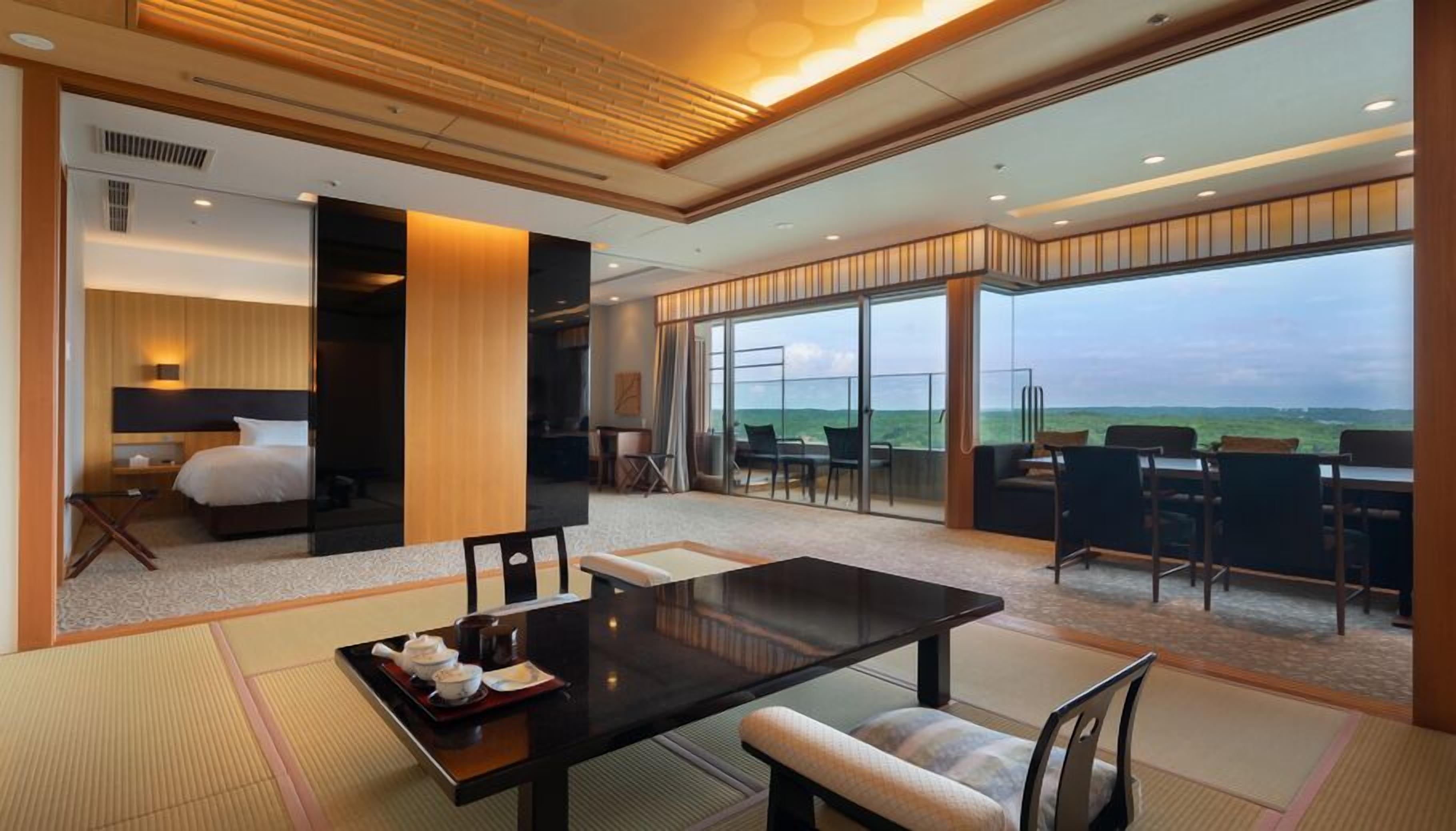 A modern hotel room with a large bed, a dining area with tatami mats, and a balcony with a view.