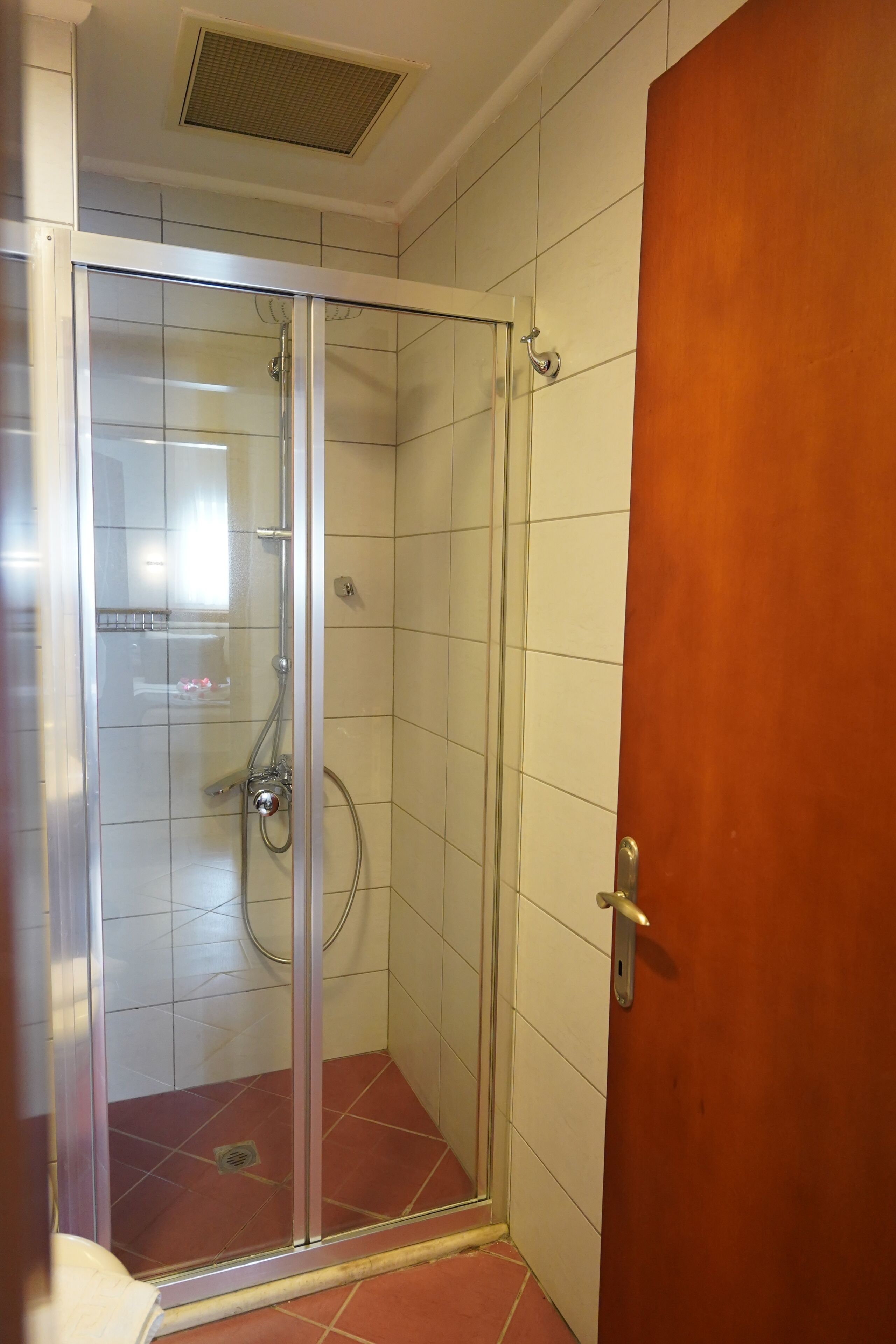 Box de chuveiro com paredes de azulejos brancos e chão em mosaico vermelho.
