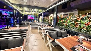 A restaurant with booths and tables, a TV screen, and a wall decorated with tropical plants. - Club Karakas Apart (Marmaris)