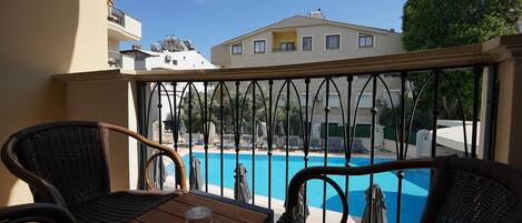 A balcony with wicker furniture, a pool, and a building in the background.
