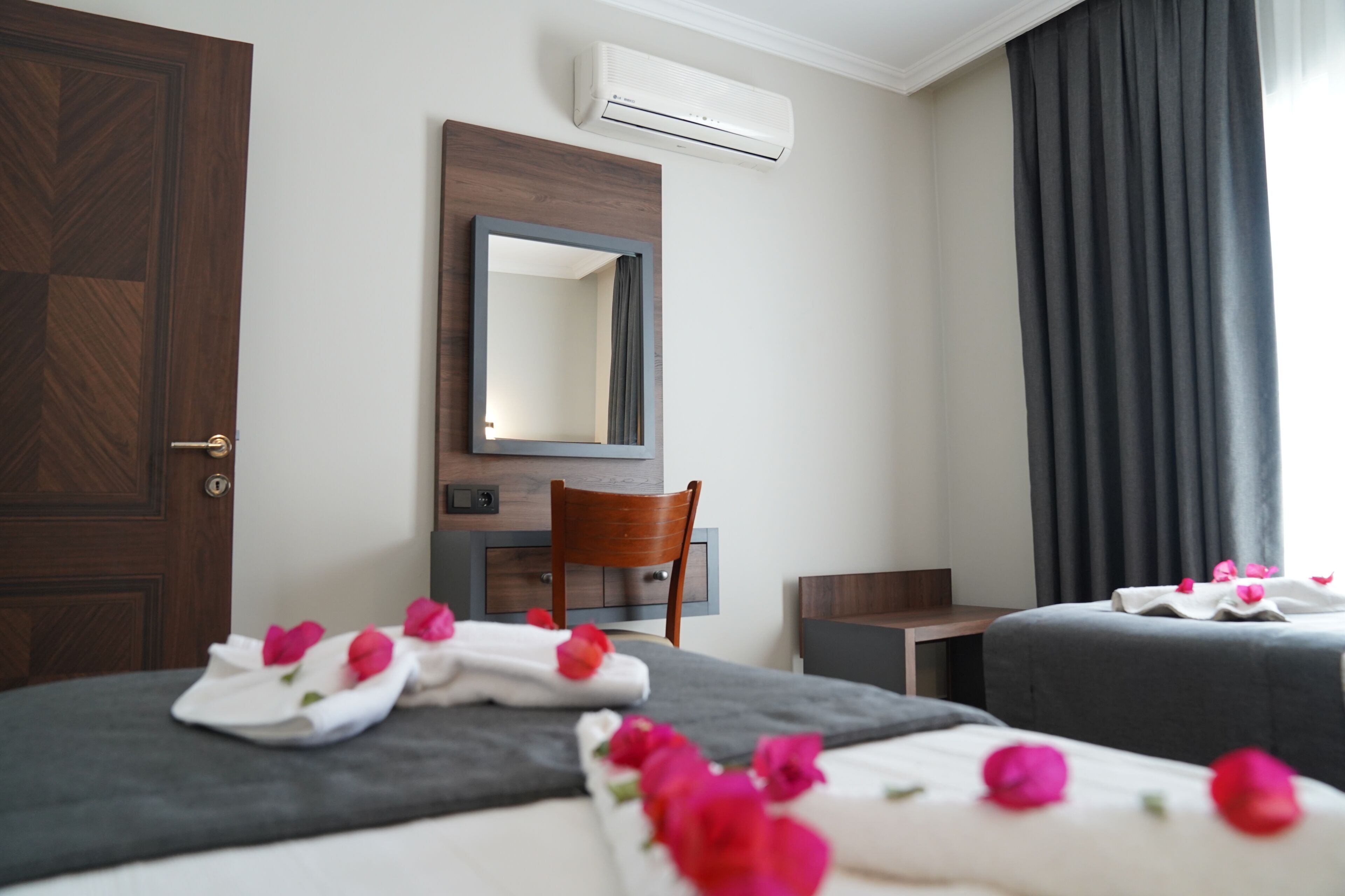 A hotel room with a bed, a desk, a chair, a mirror, and an air conditioning unit.
