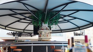 A bar area with a large umbrella, a hanging plant, and a shelf with bottles. - Club Karakas Apart (Marmaris)