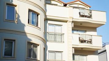 A multi-story building with balconies, windows with curtains, and a clear sky.