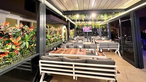 A modern restaurant with wooden tables and benches, a green wall with plants, and a TV screen in the background. - Club Karakas Apart (Marmaris)