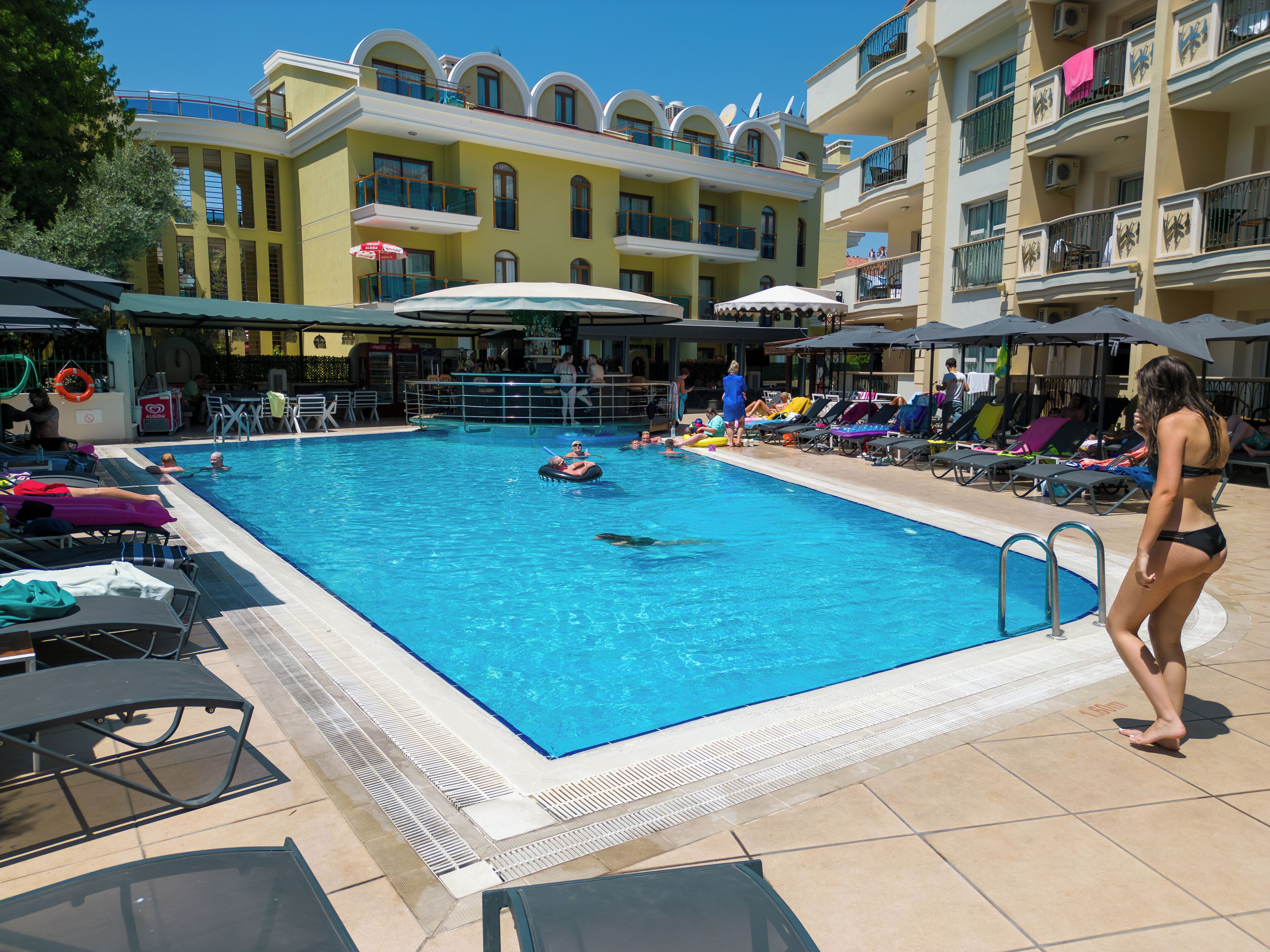 A swimming pool with lounge chairs and umbrellas, surrounded by multi-story buildings with balconies.