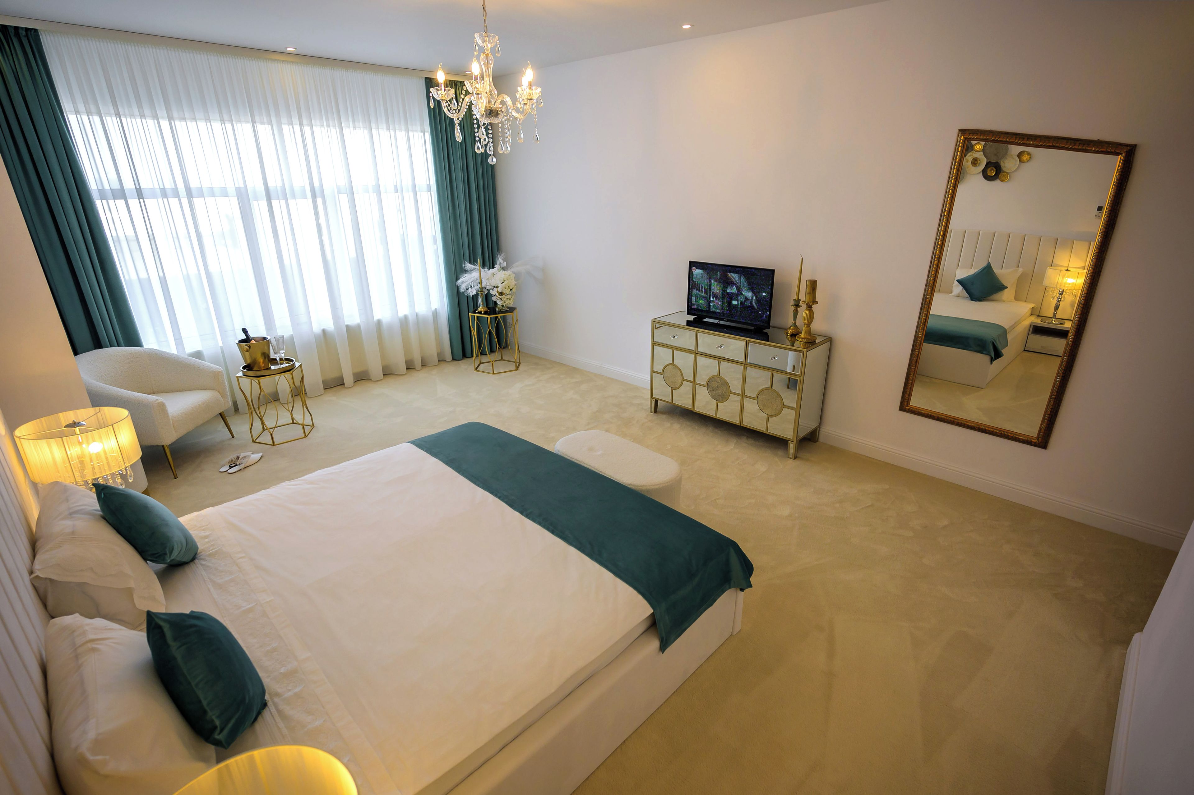 Een slaapkamer met een groot bed, een televisie, een dressoir, een stoel en een spiegel.
