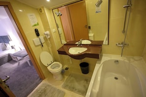 A bathroom with a toilet, sink, mirror, shower, and a trash bin. - Queen Vera Hotel (Constanta)