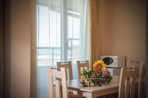 Un comedor con una mesa dispuesta para dos personas, un ramo de flores y un microondas sobre la mesa.