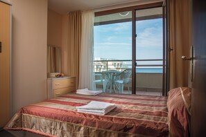 A hotel room with a bed, a desk with a chair, a balcony with a table and chairs, and a view of the sea. - Prestige City 2 (Primorsko)
