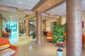 A spacious lobby with a central staircase, orange seating, and potted plants. - Prestige City 2 (Primorsko)