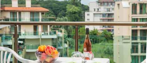 A balcony with a table set for two, a bowl of fruit, a wine bottle, and a glass.