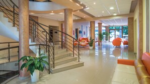 A spacious lobby with a staircase, seating area, and potted plants. - Prestige City 2 (Primorsko)