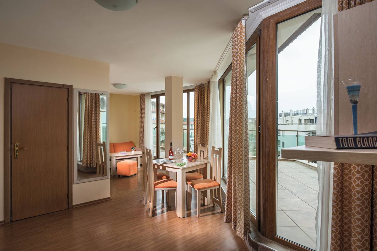 Habitación de hotel con comedor, un ventanal con cortinas y vistas de la ciudad.