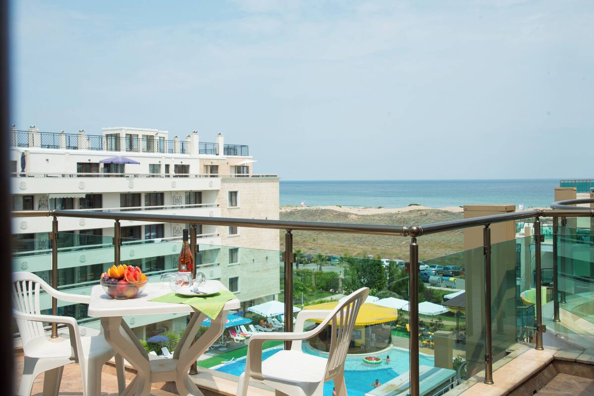 Un balcón con mesa, sillas, frutero y vista al mar y la playa.