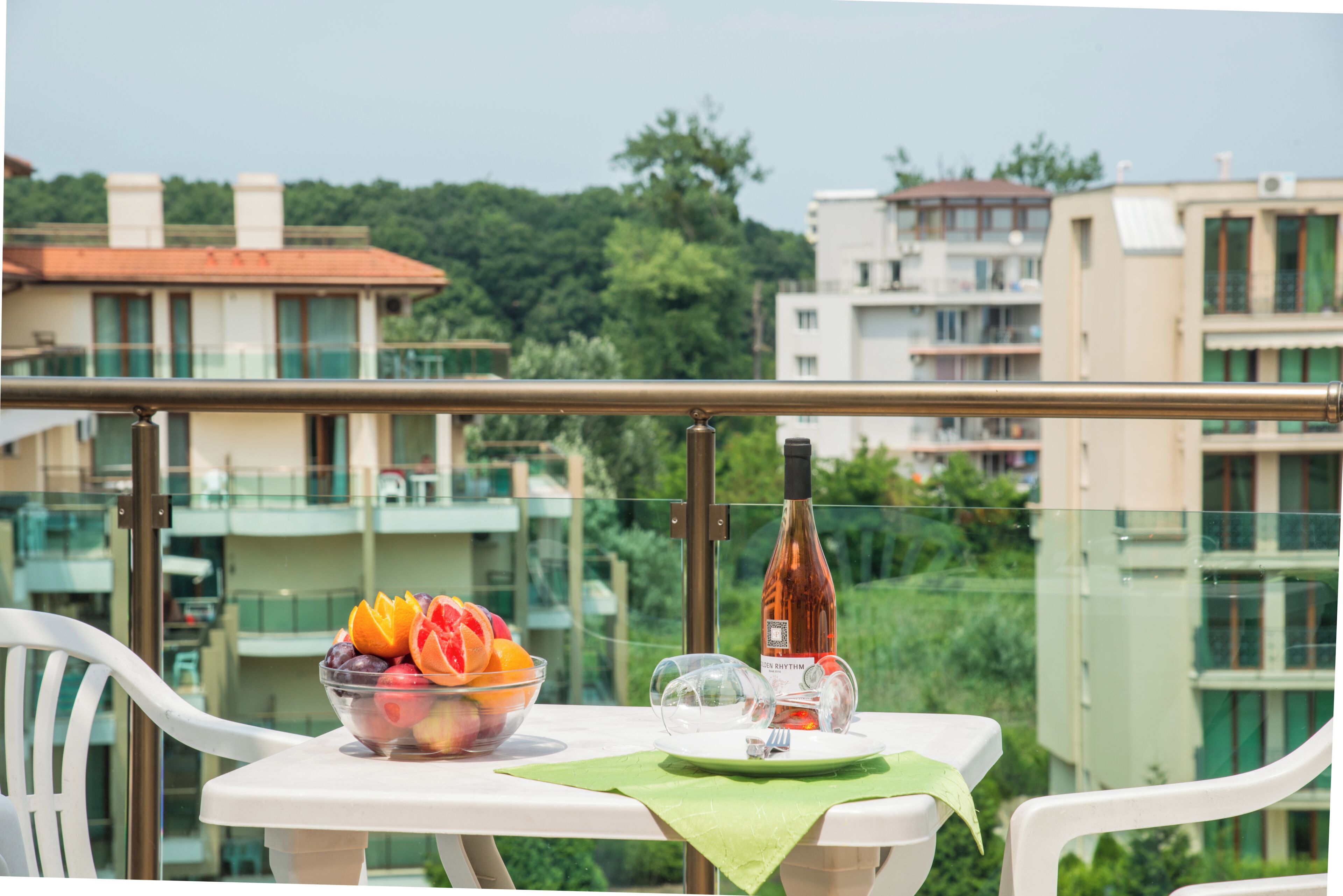 A balcony with a table set for two, a bowl of fruit, a wine bottle, and a glass.