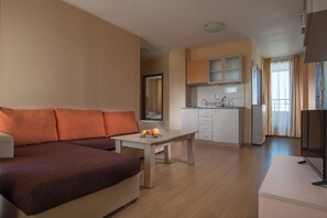 Una sala moderna con un sofá, una mesa de comedor con fruta, una zona de cocina con armarios y un televisor.