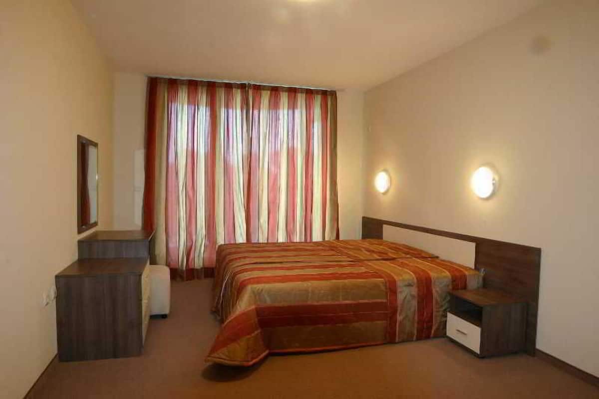 A hotel room with a bed, bedside tables, a mirror, curtains, and wall-mounted lights.