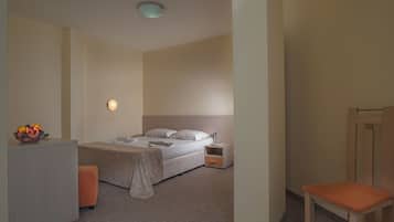 A hotel room with a bed, bedside table, chair, and a fruit bowl.