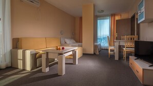 Une chambre d’hôtel avec un canapé, une table, une télévision et un balcon doté de rideaux.