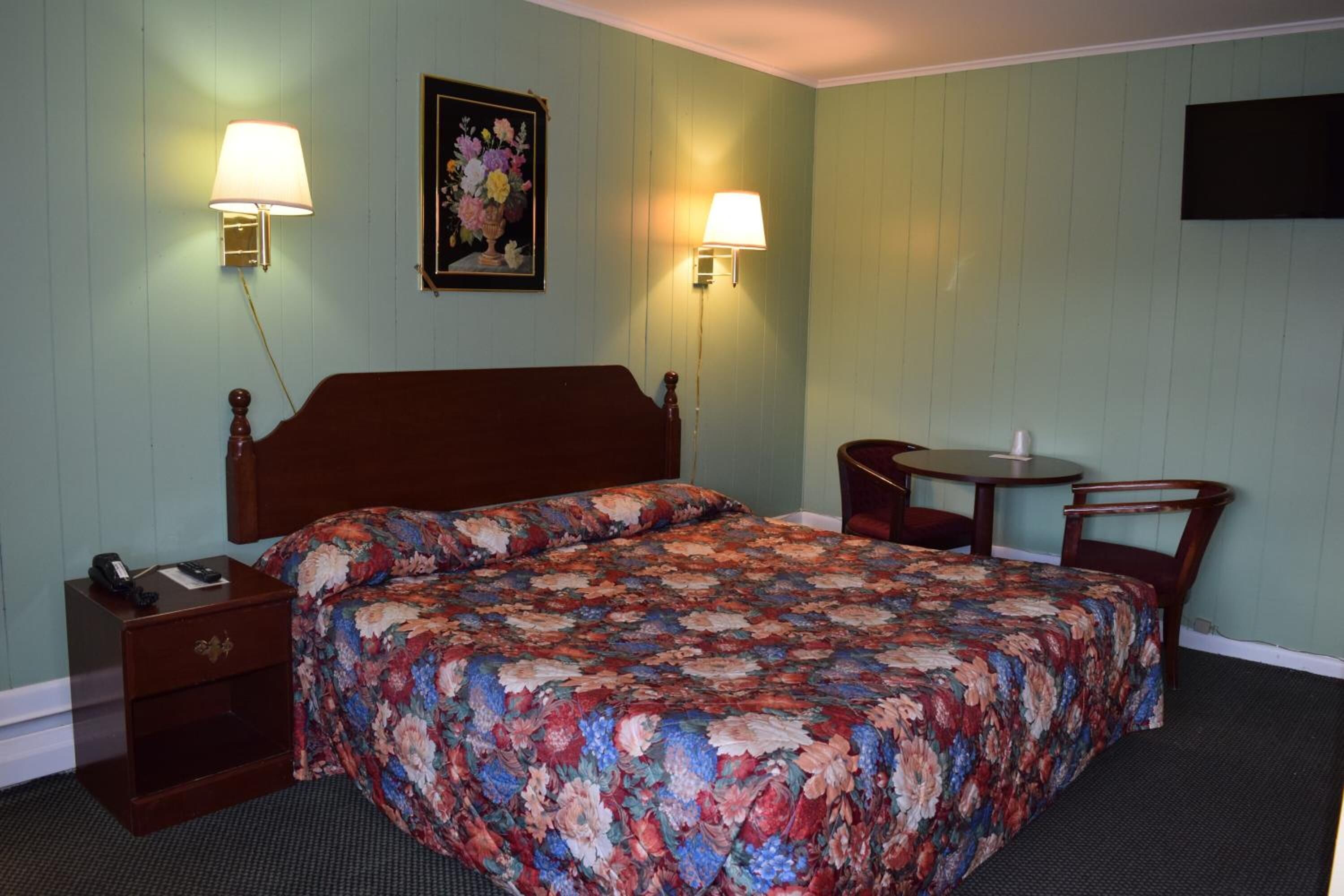 Habitación de hotel con una cama de madera, dos lámparas de noche, una mesita y una silla.