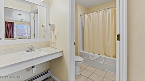 Een badkamer met een witte wastafel, spiegel en toilet. Er is een douchegordijn en een handdoek aan de muur.