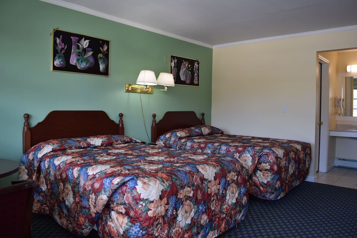 A room with two beds, a nightstand, a lamp, and two wall-mounted paintings.