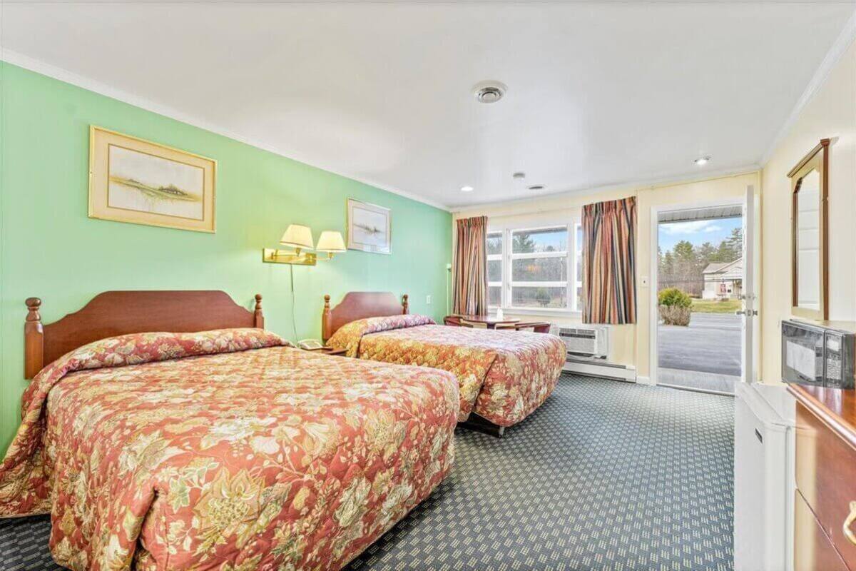 A hotel room with two beds, a desk, a chair, a TV, and a window with curtains.