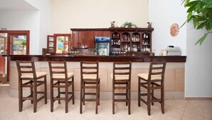 A bar area with wooden chairs, a bar counter, and a refrigerator. - Golden Sun (Karpathos)