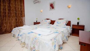 A double bed with floral bedding, two bedside tables, a wall-mounted air conditioner, and a red flower decoration. - Golden Sun (Karpathos)