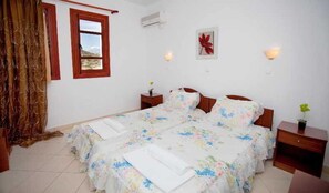 A bedroom with a bed, curtains, a window, a wall-mounted air conditioner, and a wall-mounted light fixture. - Golden Sun (Karpathos)